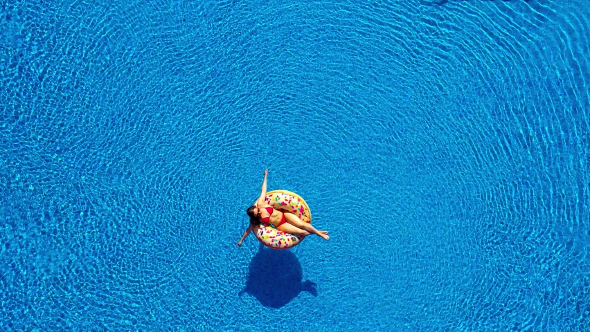 Aerial view of man dives into the the pool while girl is lying on a donut pool float Royalty-Free Stock Footage #1065935047
