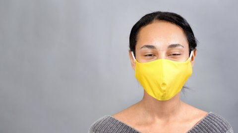 Close up portrait of smiling mixed-race woman wearing yellow medical mask. Gray background. Copy space. Illuminating yellow and ultimate gray . 4K UHD