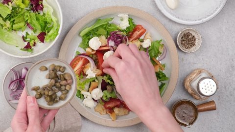Time lapse preparation of healthy vegetable salad with tomatoes, mozzarella cheese, capers, croutons and red onion slices. Female chef cooking salad. Top view