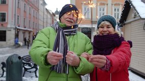 Senior couple with burning sparklers celebrating anniversary on winter city center street. Elderly family holding bengal lights enjoying Christmas eve. Active retired pensioners celebrating birthday - Powered by Shutterstock - Get 15% off with code: PIKWIZARD15
