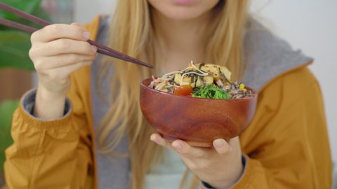 A young woman enjoys her dinner in a beautiful cafe where poke bowls are served. Fast and healthy. Trendy food concept