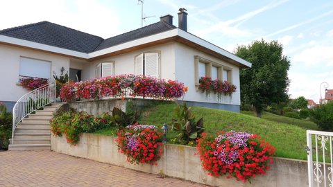 WETTOLSHEIM, FRANCE - AUGUST 18, 2019: Small cozy cottage, many colorful flowers around, fine gardening, green lawn in front. Beautiful one storey house at Wettolsheim village