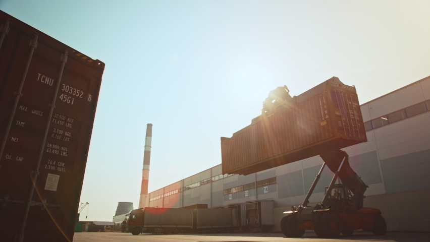 Modern Container Handler Carrying a Large Red Steel Shipping Cargo Storage Container in a Shipyard Terminal. Driver Operating the Handling Equipment is Loading the Crate in the Logistics Center. | Shutterstock HD Video #1065943381