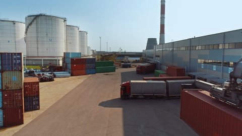 Aerial Drone Footage of a Container Handler Carrying a Large Red Shipping Cargo Container in a Shipyard Terminal. Driver of the Machine is Loading the Crate in the Logistics Center Depot.