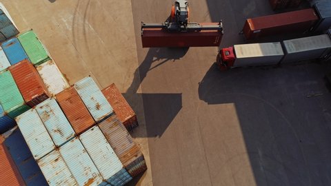 Aerial Drone Footage of a Container Handler Carrying a Large Red Cargo Container in a Shipyard Terminal. Driver of the Machine is Loading the Crate in the Logistics Center Depot. Top Down View.