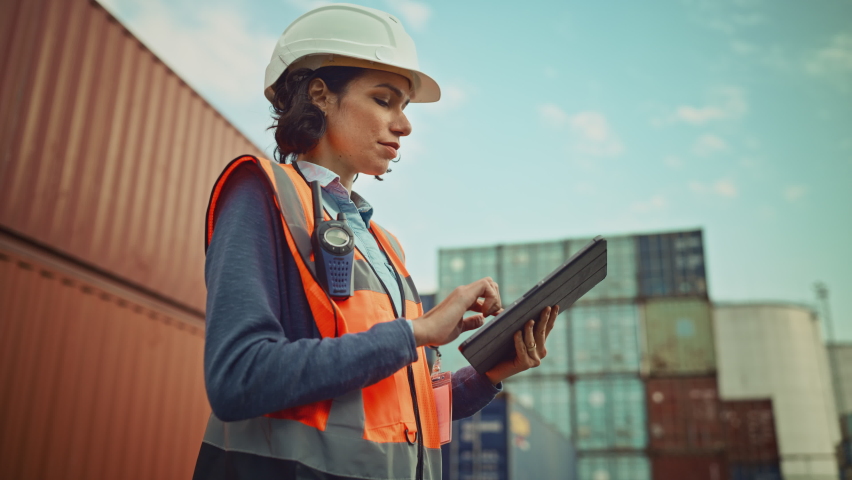 Smiling Portrait of a Beautiful Latin Female Industrial Engineer in White Hard Hat, High-Visibility Vest Working on Tablet Computer. Inspector or Safety Supervisor in Container Terminal. Royalty-Free Stock Footage #1065943453