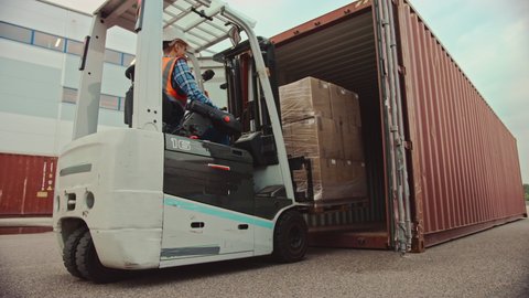 Forklift Driver Loading a Shipping Cargo Container with a Full Pallet with Carboard Boxes in Logistics Operations Port Terminal. Tracking Shot from the Side Shows How Pallet is Brought by the Machine.