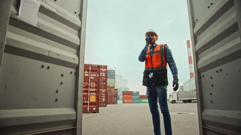Handsome Industrial Engineer and African American Supervisor in Hard Hats and Safety Vests Opening a Shipping Cargo Container in Logistics Terminal. Both Colleagues Look Happy When Opening the Doors.