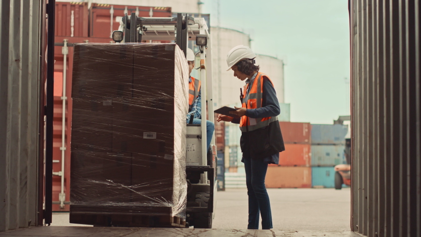Forklift Driver Loading a Shipping Cargo Container with a Full Pallet with Boxes in Logistics Port Terminal. Latin Female Industrial Supervisor and Safety Inspector with Tablet Managing the Process. | Shutterstock HD Video #1065943537
