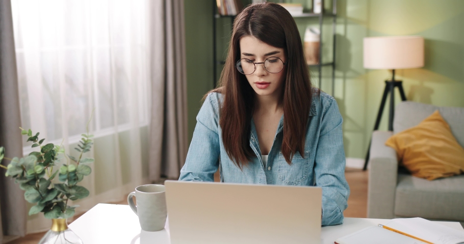 Camera approaching serious concentrated relaxed young Caucasian beautiful businesswoman sitting at table in cozy office typing on laptop, working and drinking coffee or tea, close up concept | Shutterstock HD Video #1065946690