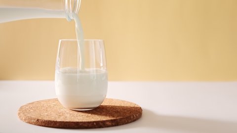 Pouring milk in glass from a bottle on a light neutral background with space for text, copy space. Glass of milk in slow motion. 