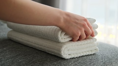 Woman hands putting stack of fresh clean white bath towels on the bed. Cleaning service.  