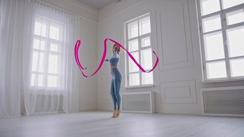 Slender young woman gymnast is spinning rapidly with bright gymnastic ribbon