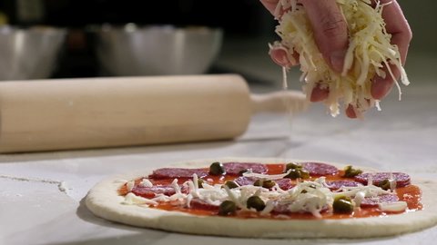 Professional baker prepares traditional Italian pizza. Cooking pizza in a restaurant in the kitchen. the cook pours grated cheese on the raw dough. the process of making pizza in a pizzeria.