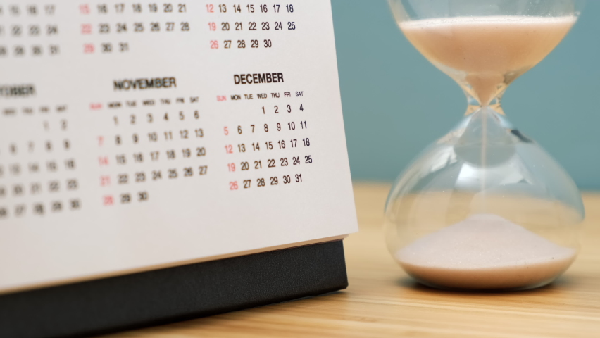 Close up of a calendar and hourglass on wooden table. Concept of starting of new year. Royalty-Free Stock Footage #1065955315