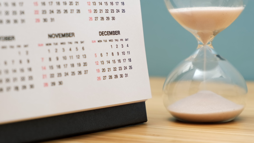 Close up of a calendar and hourglass on wooden table. Concept of starting of new year.