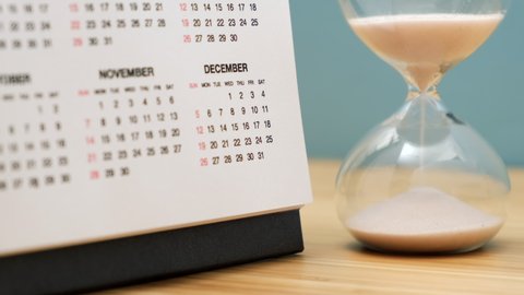 Close up of a calendar and hourglass on wooden table. Concept of starting of new year.