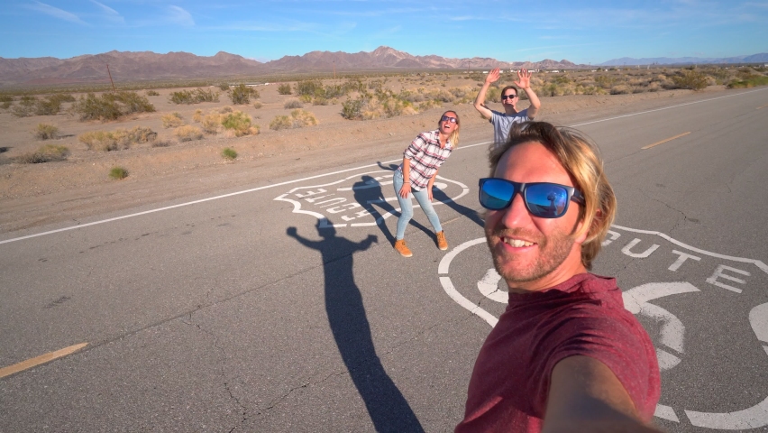 Young people travelling on a road trip taking cool selfies with Route 66 sign on the road. People travel concept. Slow motion 