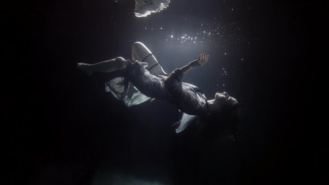 The woman is under water, her body in a dress is beautifully floating and spinning along with the bubbles. The tissue develops under water. She makes smooth movements. Swims like a mermaid under water