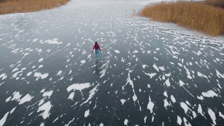 Aerial view. A young woman is skating on a frozen lake.