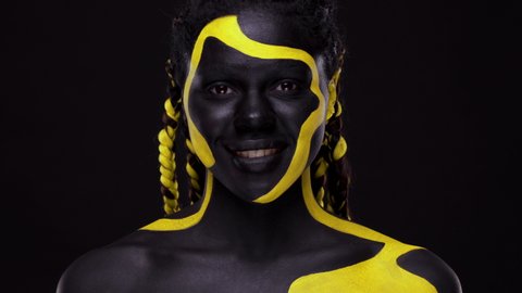 Face art. Woman with black and yellow body paint. Young african woman with colorful body paint.