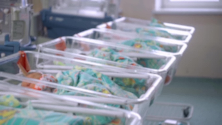 Blurred view of interior Maternity Hospital, Newborn Babies in Cots. The Nurse takes care of the Child, covers it with a Blanket and puts on a Hat Royalty-Free Stock Footage #1065967645