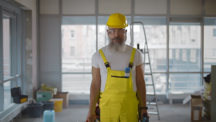 Senior multi-armed builder in overall and hardhat doing renovation. Funny portrait of aged bearded construction worker with many arms holding tools and smiling Royalty-Free Stock Footage #1065970645