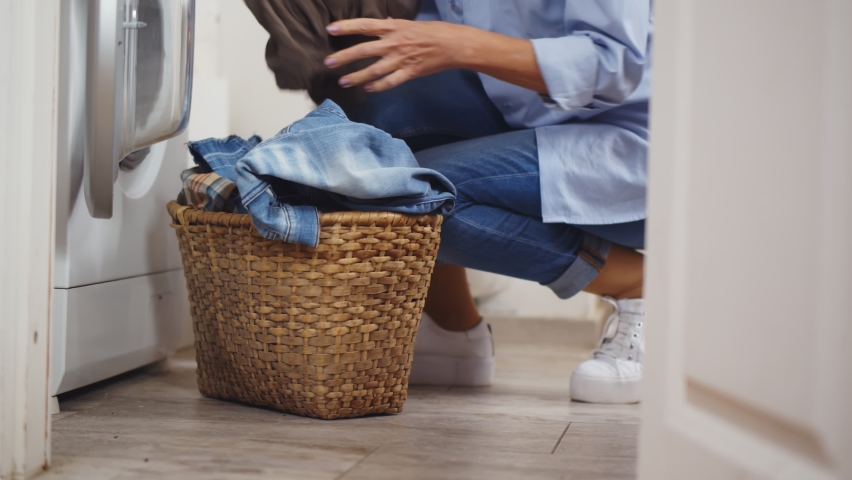 Senior woman loading dirty clothes into washing machine. Side view of mature housewife putting clothes in washing machine at bathroom doing laundry at home | Shutterstock HD Video #1065970672