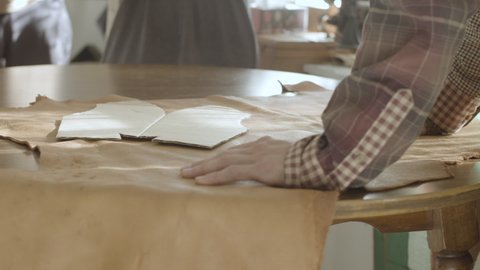Zoomed in video of a person, using sample to put marks and measurements on leather, as it needs to be cut further in shape of leather moccasins 