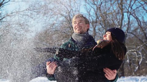 Happy Couple Having Fun in Winter Forest, Playing in Snow. Cheerful Man in Love Holds His Girlfriend in His Hands. Lovers, Positive Emotions and Family. Valentine's Day. Slow motion.