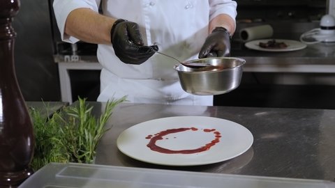 Close-up of the chef pouring strawberry and red wine sauce on a plate, serving meat dishes in the restaurant kitchen.