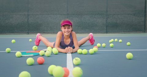 Cute girl laying on tennis court as a bunch of tennis balls rolling towards her. Female player wears colorful clothes. High quality 4k footage