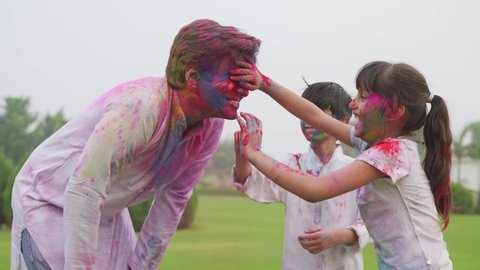 cute little girl and boy putting powdered colours on their fathers face also they are looking joyful during the occasion of holi festival