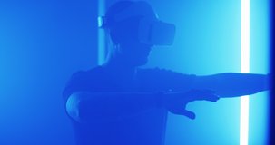 Pan around view of man in VR headset gesticulating and interacting with virtual reality while standing amidst flickering blue lamps