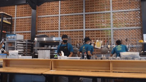  People in uniform and face masks working at open kitchen in restaurant. Bali-December-2020