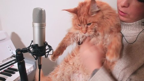 Talented woman with cat Maine Coon sings song in microphone in music studio. She opens her mouth to pronounce text. Creating new sound. Creative leisure time alone.