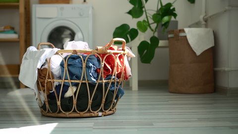 Basket of dirty clothes is standing on floor in laundry room at home spbd. Close-up view of container filled with clothing stands on background of washing machine indoors. Picture of house during