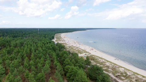 Aerial view of crowded pandemic beach goers at island Baltic sea sun tanning bathing close together sandy beach resort island happy summer day with family friends playing beach volley ball forest