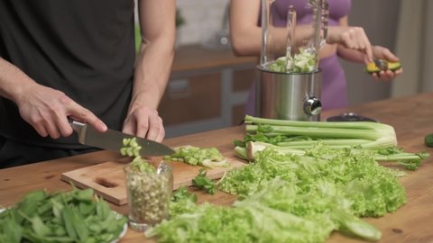 Man cuts fresh celery on a cutting Board at the home kitchen. Woman helping cooking vegetable cocktail. healthy food concept
