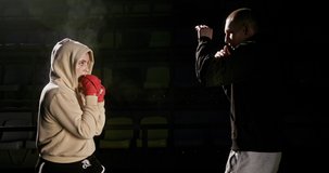 Young woman kickboxer training in the ring. Young woman kickboxer training in the ring with a male boxing opponent or personal trainer in a dimly lit gym in a fitness and active lifestyle concept.