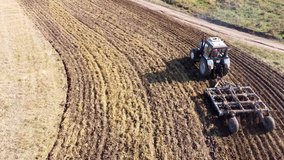 Wonderful video from a drone with a view of a tractor harrowing an agricultural wheat field. The village of Varzi-Yatchi, Udmurtia, Russia. Wonderful autumn landscape with agricultural machinery.