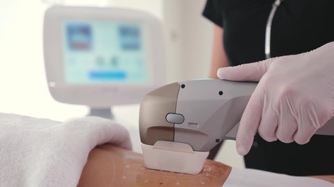 Hand of a beautician in a glove makes the procedure of hardware removal of fat from the abdomen of a client in a beauty clinic close up. The concept of extending slimness and weight loss