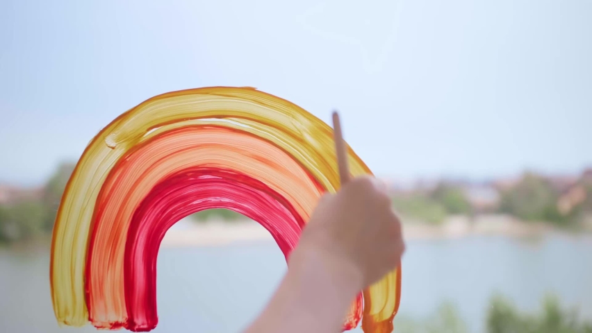Girl draws a rainbow on the window. Rainbow on the glass. Close. Front view