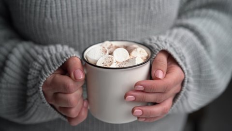 Woman holding mug with hot cocoa with marshmallow and chocolate.