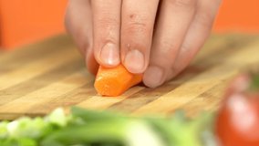 Close  view chef's hand cutting carrot  with sharp knife. Man's hand chopping carrot, macro shot. Healthy Food Concept. A young man prepares food in the kitchen. High quality 4k video.