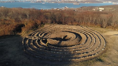 Aerial around man walks in circle lined with stones maze pagan ritual. Old Believer rite. Rock garden. Vladivostok Russia Far East best autumn cityscape. Golden horn bay. Sunny. Symbol of superstition