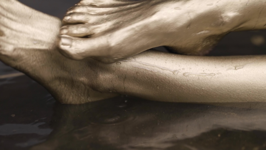 Naked feet of a female model with gold-colored skin is in the water in the water, posing. | Shutterstock HD Video #1066025122