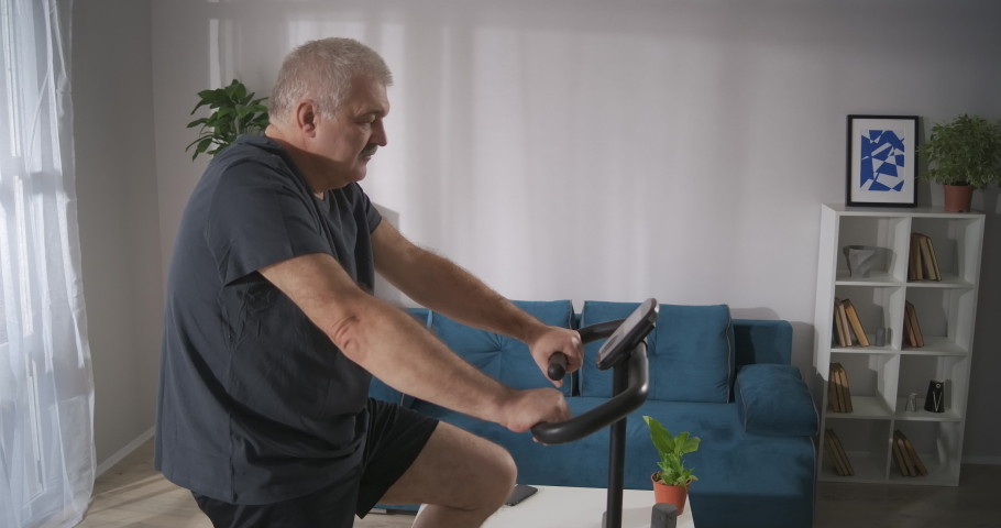 training with stationary bicycle in home, middle-aged man is keeping fit and losing weight by workout