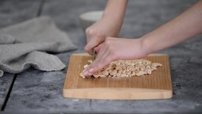 Closeup: Womans hands with knife cut cashew nuts on a cutting board in a kitchen.