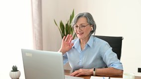 Mature businesswoman having virtual meeting, online video conference at laptop, chatting with teammates or family, meeting friends online at the home office. Senior lady looks at webcam and talking